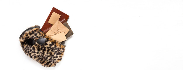 Flat lay set of women's accessories in a bag of fur leopard pattern and tropical leaves on a light background. Fashion, trend and shopping concept long banner