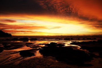 Fototapeta na wymiar Sky with deep hanging storm clouds and wet sludge during low tide swathed in yellow and red bright light during sunset on tropical island Ko Lanta, Thailand