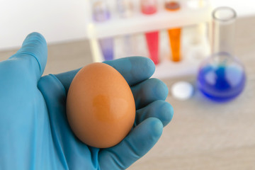 egg in the hand of the laboratory assistant against the background of laboratory equipment with preparations for analysis