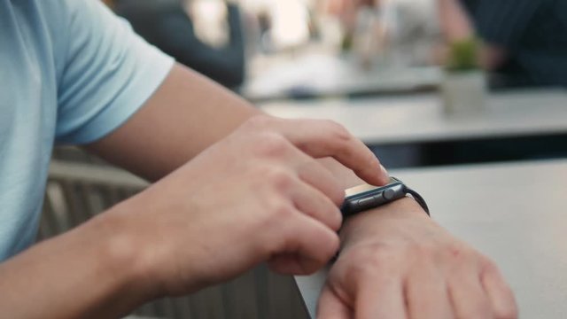 Close - up shot of male's hand uses of wearable smart watch while sitting at outdoor cafe