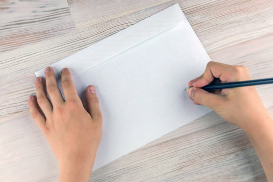 boy signs blank envelopes lying on a wooden table, close-up, low contrast, haze effect