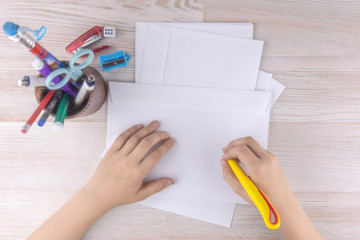 child is going to write an address on an envelope for Santa Claus, a wooden table, writing materials beside