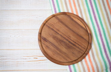 Round pizza cutting board and striped tablecloth on white wooden background. Top view. Copy space and mock up.