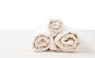 Obraz na płótnie Canvas Rolled white towels on white wooden table isolated on white background. Copy space and top view. Bathroom objects for shower body treatment. Selective focus