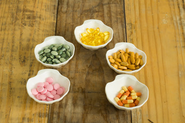 Drugs in the form of capsules, tablets and gelatin in oyster-shaped bowls on dirty wooden background