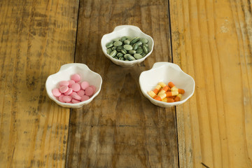 Drugs in the form of capsules, tablets and gelatin in oyster-shaped bowls on dirty wooden background