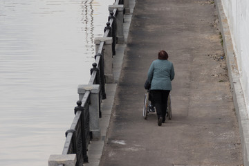 Woman helping to roll a wheelchair with a person along the promenade