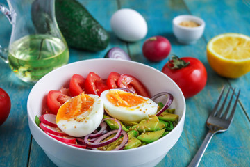 healthy bowl with boiling egg halves tomatoes avocado red onion radish arugula sesame seeds  on blue wooden table close up