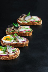 smorrebrod sandwiches  with herring rye bread boiling eggs cucumber sliced radish green onions on black background vertical orientation