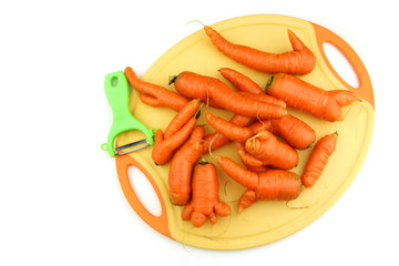 Bio Karotten Möhren ungenormt mit Händen und Beinen auf Schneidbrett mit Schäler