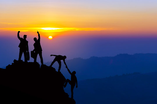 Teamwork friendship hiking help each other trust assistance silhouette in mountains, sunrise. Teamwork of four men hiker helping each other on top of mountain climbing team beautiful sunrise landscape