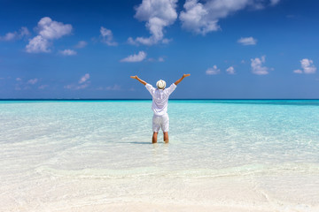 Fototapeta na wymiar Man in white summer clothes stands on a tropical beach with turquoise sea and enjoys his freedom