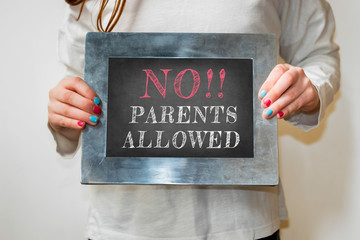 Child holding a blackboard with the text no parents allowed