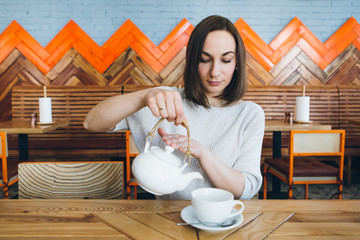 Woman pours green tea from a teapot into a Cup in a cafe