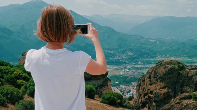 Back view female hipster tourist taking photo of amazing mountain landscape using smartphone