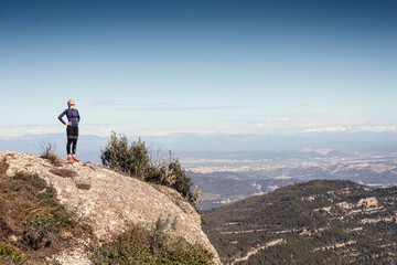 Trail runner standing and taking a break while looking landscape from mountain peak.