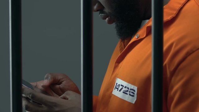 African-American prisoner scrolling on smartphone, forbidden items in jail