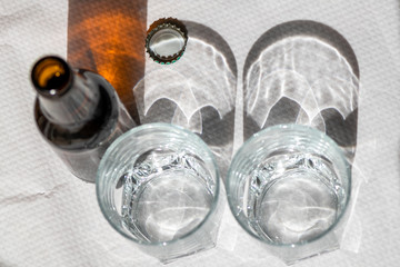 Two cristal glasses and one beer bottle on a white paper tablecloth. Sunny scene with shadows. Concept- share.