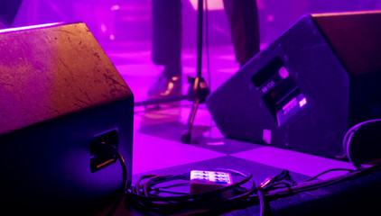 Stage monitor speakers and cables in purple ambient light at band live gig