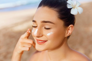 Skincare. Beauty Concept. Young pretty woman applying sun cream  and touch own face. Female in hat...