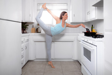 Joyful woman cooking and multitasking with yoga pose, healthy living positive attitude, wellness, wellbeing, happiness and positivity