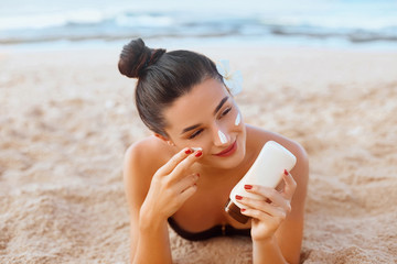 Skin care. Sun protection. Beautiful Woman In Bikini apply sun cream on Face. Woman With Suntan Lotion On Beach. Portrait Of Female Holding Moisturizing Sunblock.The Girl Uses Sunscreen for Her Skin.