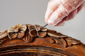 Renovation of old furniture as an antique Victorian old wooden armchair. Excition and cleaning the old varnish and paint with chisel from the decorative elements of carving on the back of the chair.