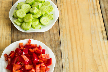 Sliced ​​cucumber and red pepper in plates on dirty wooden background