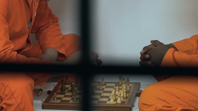 Multiracial male cellmates playing chess in spare time, prison entertainments