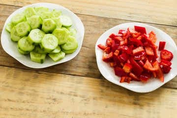 Sliced ​​cucumber and red pepper in plates on dirty wooden background