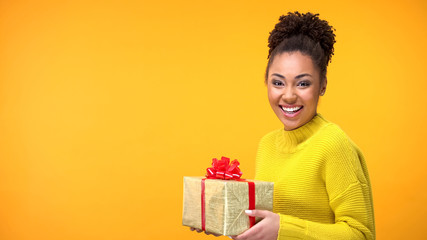 Joyful afro-american female holding present on bright background, happiness