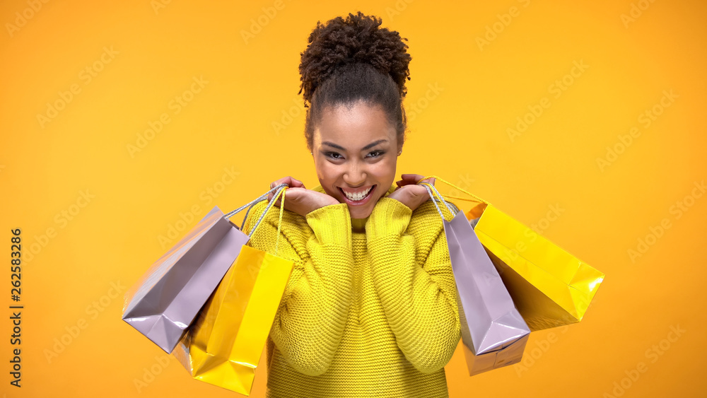 Wall mural excited young woman in stylish yellow sweater holding shopping bags, discount