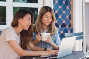 Asian young women in smart casual clothes working sending email on laptop and drinking coffee while sitting in cafe. Lifestyle women communication and working in coffee shop concept.