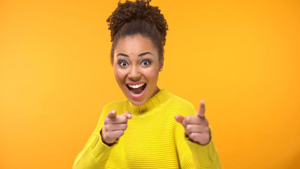 Inspired young woman pointing hands in camera on yellow background, motivation