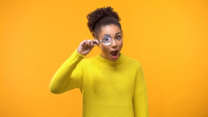 Curious afro-american woman looking magnifying glass, having fun, surprise
