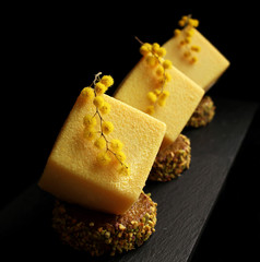 Yellow easter orange mousse textured desserts on pistachio sponge cake slices with mimosa flowers