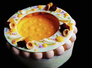 Colorful fancy orange and hazelnut cheesecake isolated on black background
