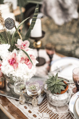 Obraz na płótnie Canvas Beautiful glasses, candles, flowers stand on a fruitful decorated table in rustic boho style. Bright composition of flowers with a decor in the style of the rustic