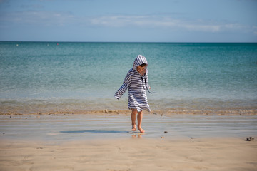 Fototapeta na wymiar little boy on playing a beach covered in dressing gown against sun burn 
