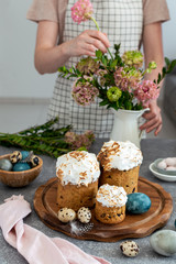 Easter table - female arranging ranunculus flowers, easter cake, milk bottle, coloured eggs, quail eggs, willow banch, vertical