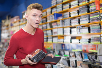 Surprised young male standing in shop with stack of DVDs