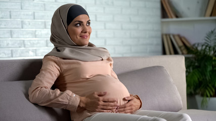 Pregnant muslim lady holding belly, guessing gender of unborn child, maternity
