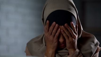 Frustrated muslim lady in hijab covering face with hands, life problems, stress