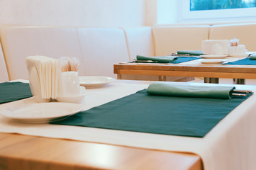 Close up dining setup with empty white plates, silver cutlery in green napkins, decorations and items served for food, arranged by catering service in a modern restaurant, cafe