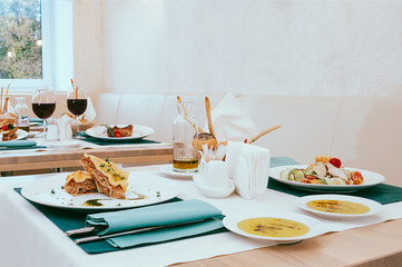 Beautiful dining setup with wine and water glasses, cutlery in green napkins, food served on white plates, arranged by catering service in a modern light restaurant, cafe. Italian European cuisine