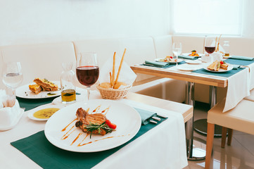 Dining setup with wine and water glasses, cutlery in green napkins, food served on white plates, arranged by catering service in a modern light restaurant, cafe. Italian European cuisine