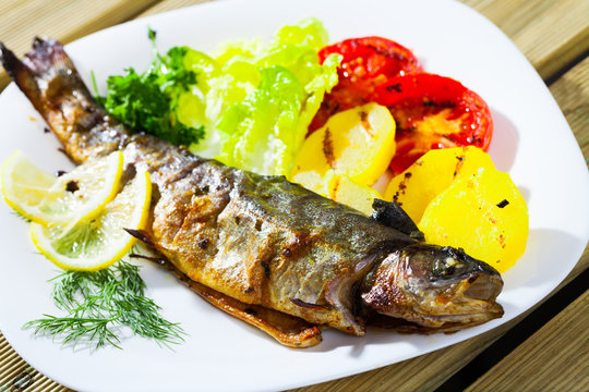 Picture of  tasty baked whole  trout  with potatoes, greens and tomatoes