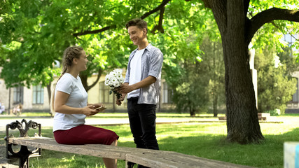 Fototapeta premium Nervous teenager presenting flowers to pretty girl in park, pick up master