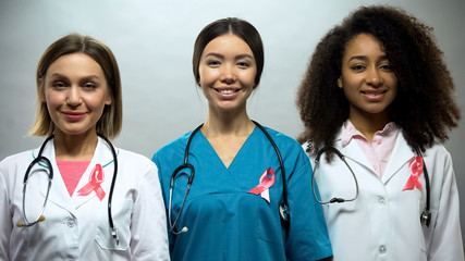 Group of smiling nurses with pink ribbons, breast cancer awareness, treatment