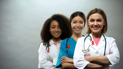 Smiling multiracial doctors with red ribbons, international AIDS awareness sign